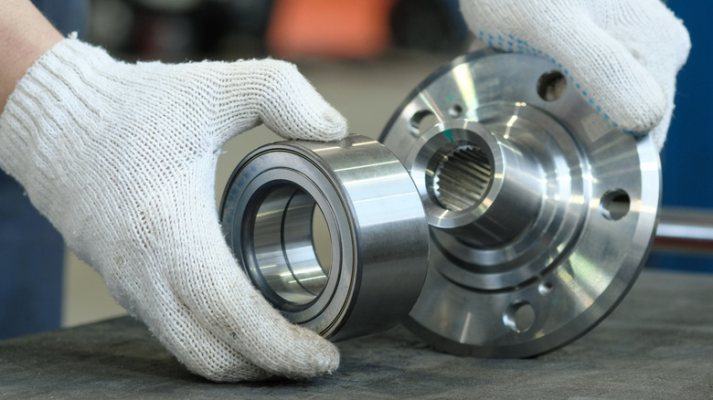 A close up of a person with white gloves handling a car part with both arns.