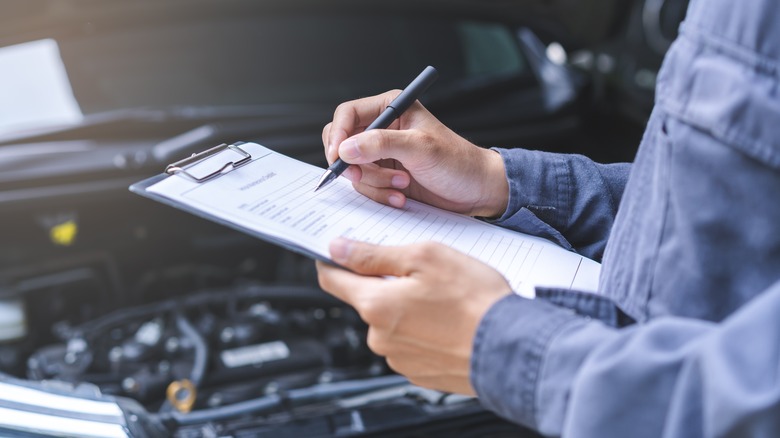 a mechanic holding a clipboard looking over a car
