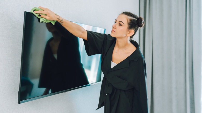 A woman dusting the top of a TV
