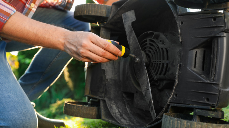 Man with screwdriver fixing lawn mower blade outdoors