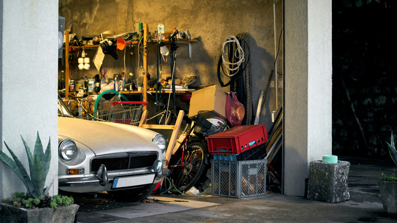A cluttered garage with a white classic car parked inside