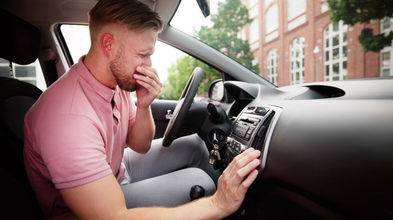 Man covering his nose inside car while checking air vent