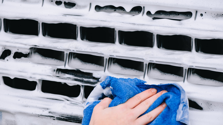 Person cleaning the front grille of a car