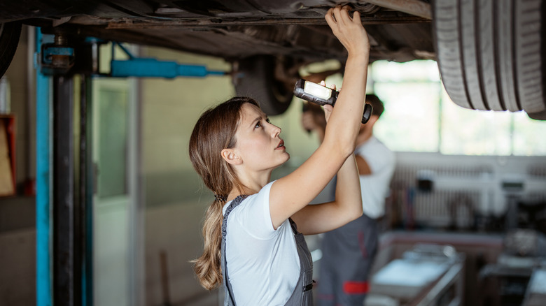 Female mechanic inspecting undercarriage flashlight