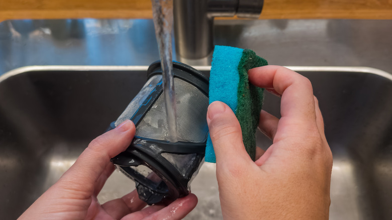 A person cleaning dishwasher filter with a sponge