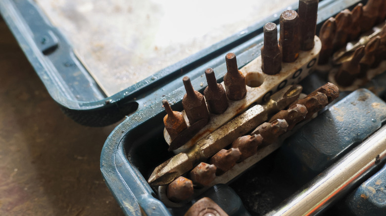 Rusty tools and drill bits in a dirty tool box.