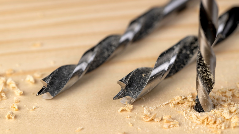 Drill bits drilling into a wooden board.