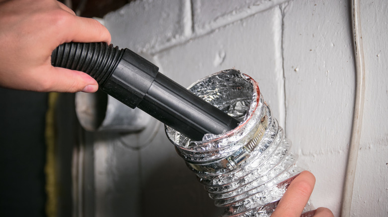 Person cleaning a dryer's vent tube with a vacuum