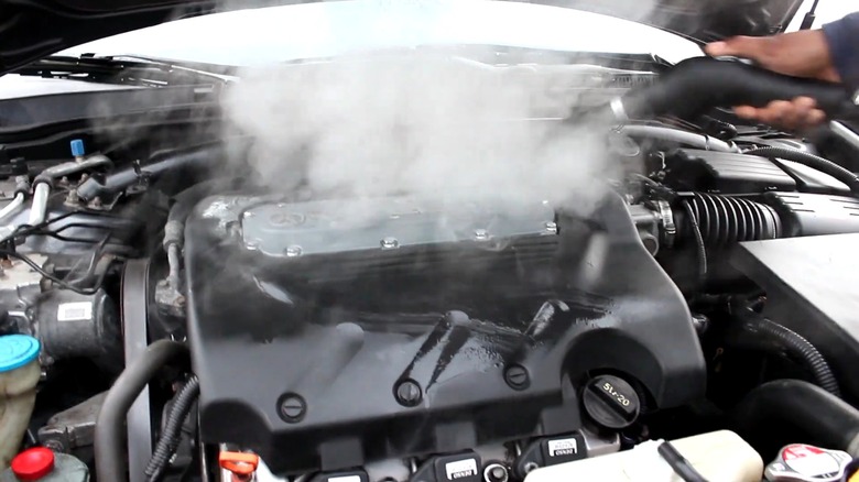 A person using a steam cleaner on a car engine.
