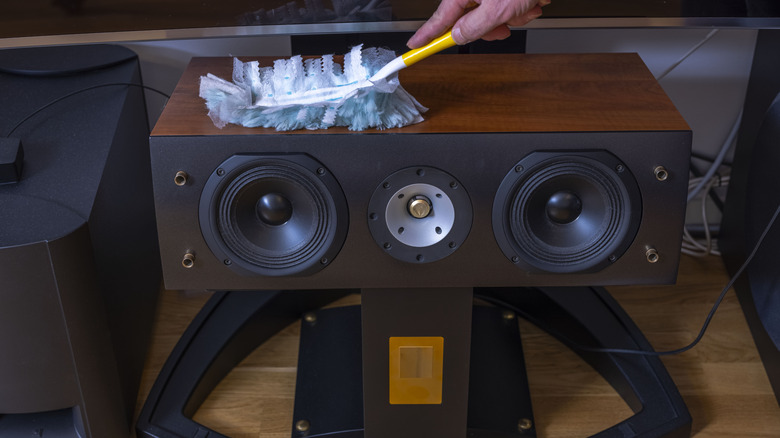 Close-up of hand cleaning speaker cabinet with soft-bristled brush