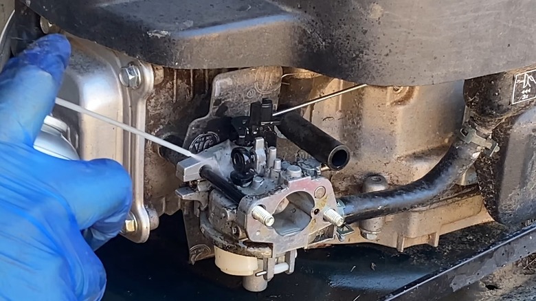 A Person Spraying The Exterior Of A Lawn Mower Carburetor With Cleaner