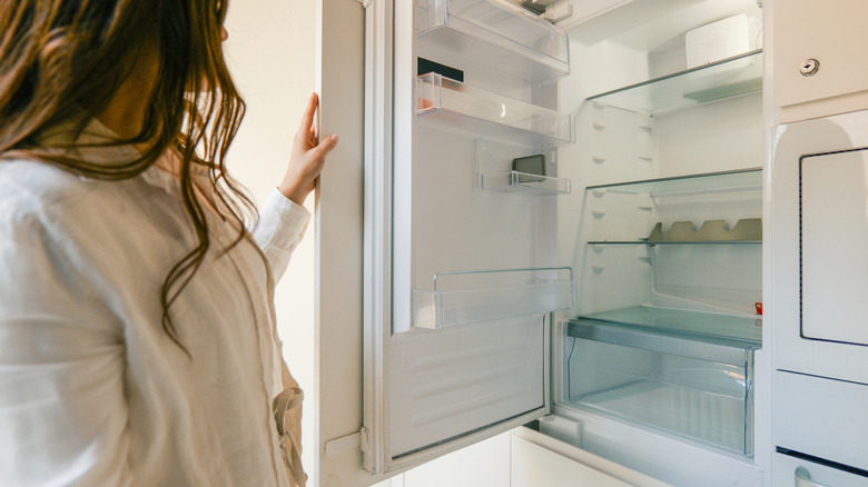 A woman opening an empty refrigerator.