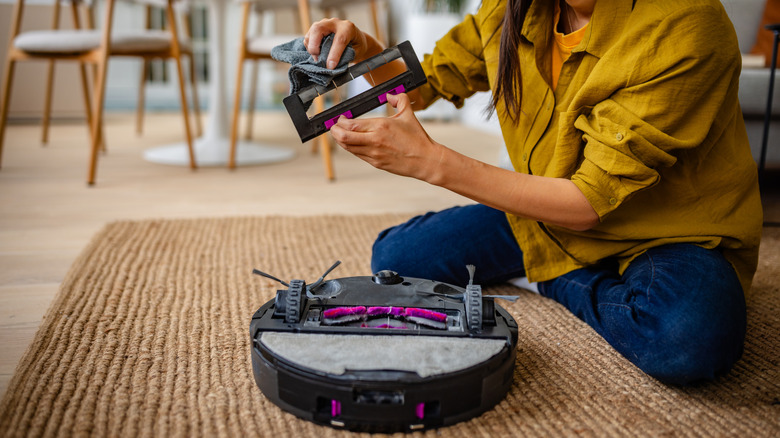 A woman removes the brush from a robot vacuum cleaner