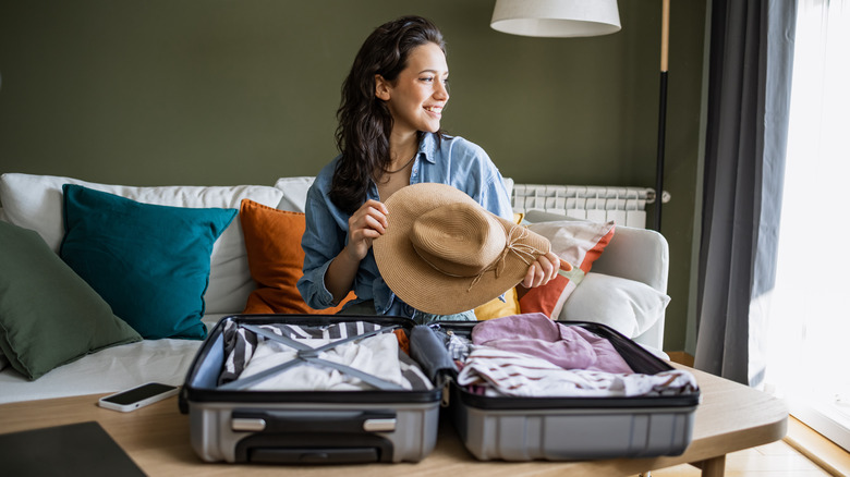 Woman packing suitcase holding a hat