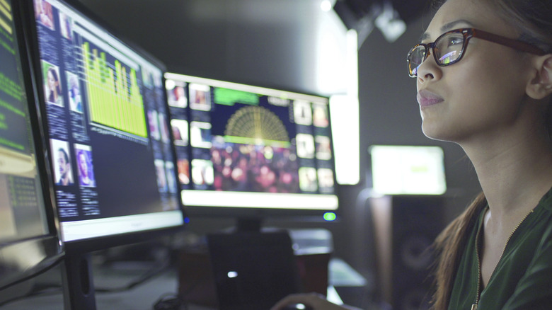 A woman is looking at multiple PC monitors