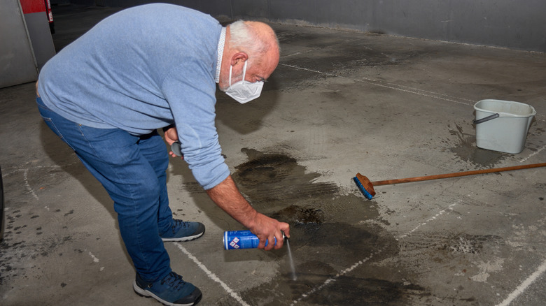 A man spraying a degreaser to an oil stain on a garage floor
