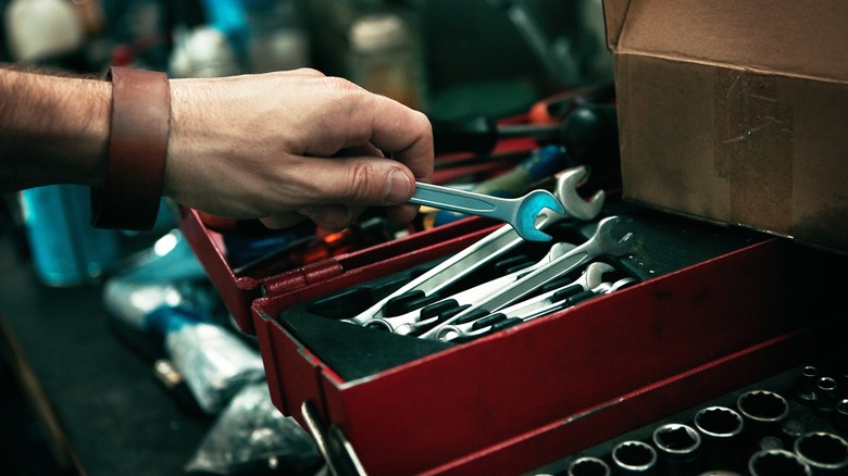 A person grabbing a wrench from a tool box.
