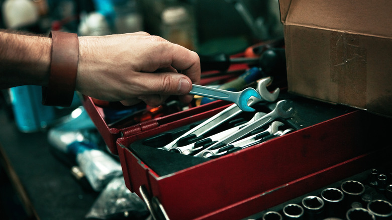 A person grabbing a wrench from a tool box.
