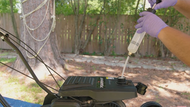 Draining gasoline from a lawn mower gas tank.