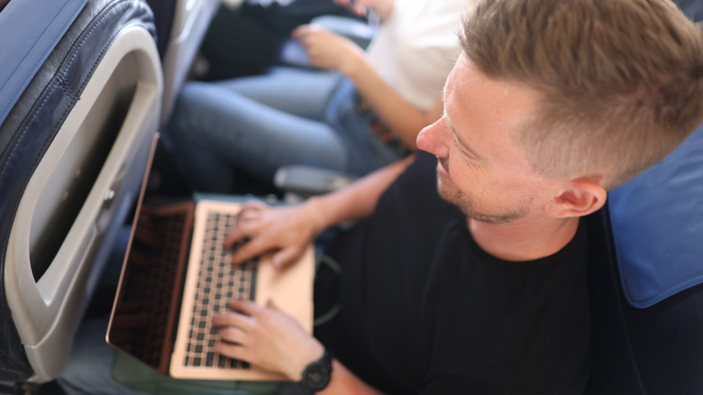 man using macbook on airplane