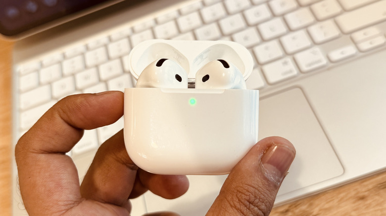 left hand holding AirPods 4 with open case lid