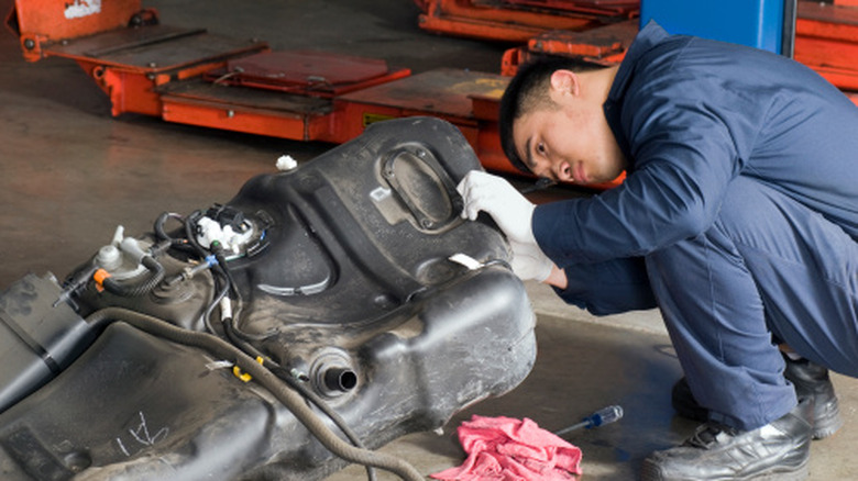 A mechanic examining a detached gas tank