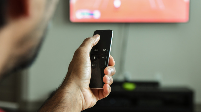 person holding Apple TV remote with TV in background