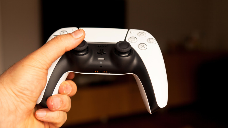 Man holding a PS5 controller in front of a black TV screen