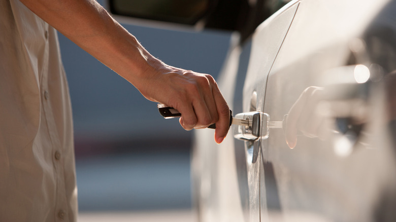 person putting car key in driver door lock