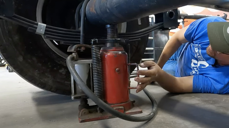 Man lying on ground lifting a trailer using a bottle jack under the axle