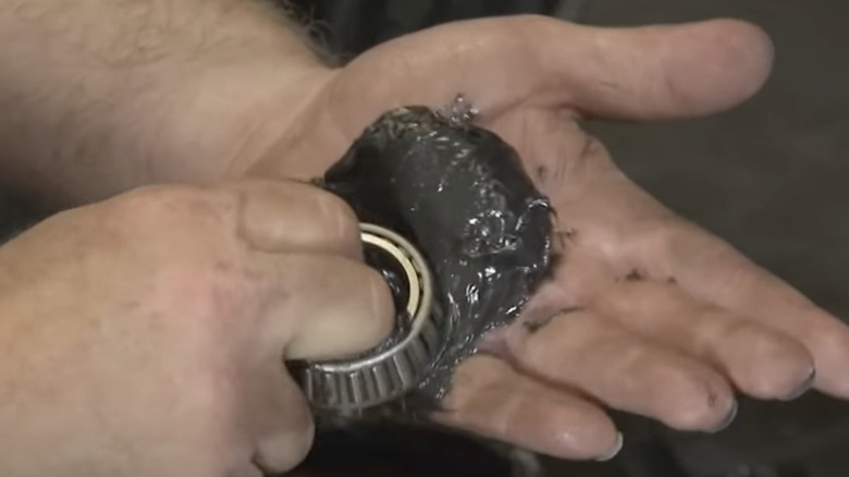 Man's hands shown packing grease into a trailer roller bearing
