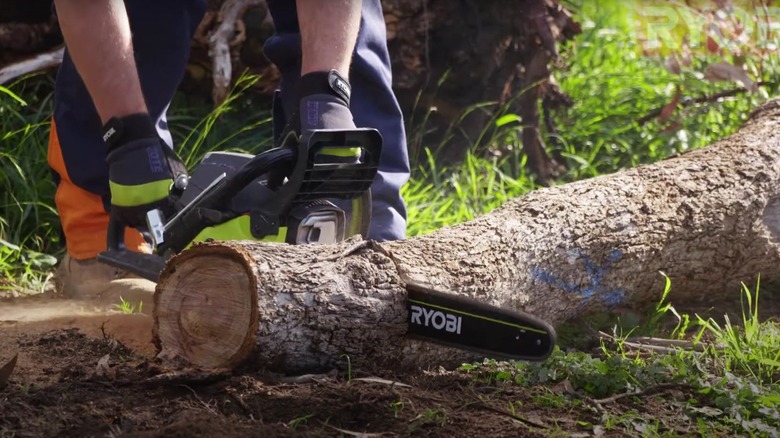 gloved worked cuts log on the ground with a Ryobi chainsaw