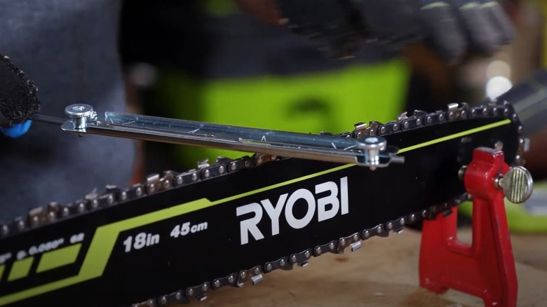 A file guide is used on a ryobi chainsaw blade, red clamp holding chainsaw upright