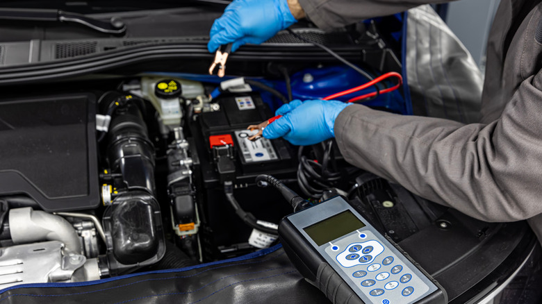 Car mechanic checking and testing automotive battery with digital electronic battery tester