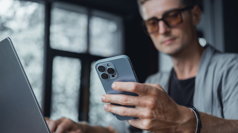 man holding iPhone in front of computer