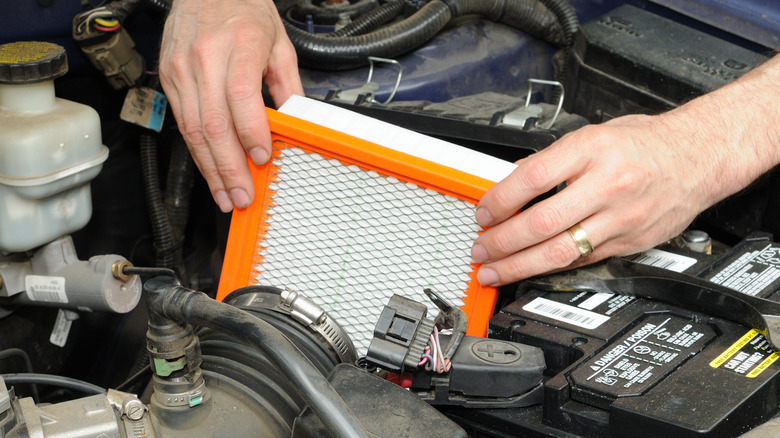 hands installing a new air filter into a car's engine compartment
