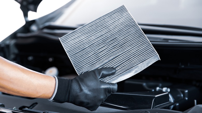 gloved hand holding a dirty card air filter over an open engine compartment