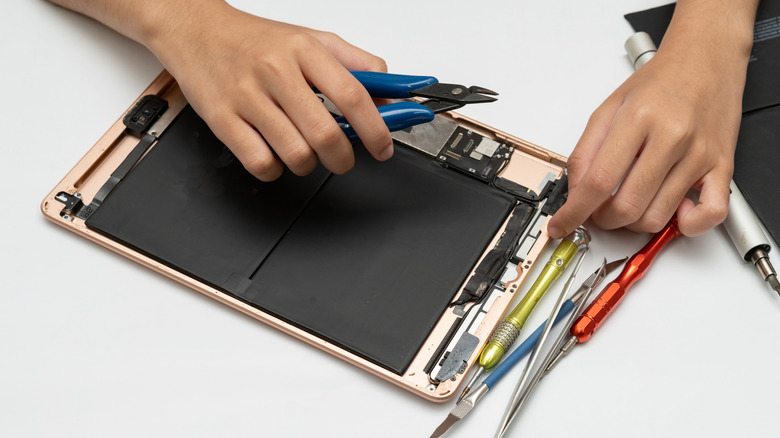 Picture of an iPad's internal components with hands holding tools