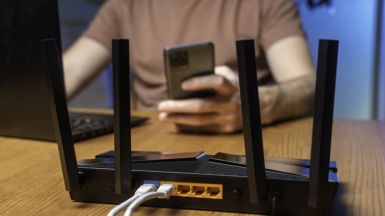 Black Wi-Fi router placed on a tabl and a man using a laptop and smartphone