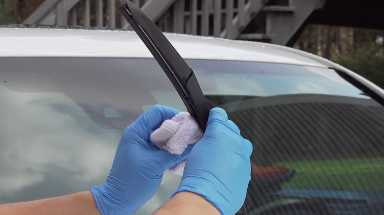 Gloved hands wiping up windshield with WD-40