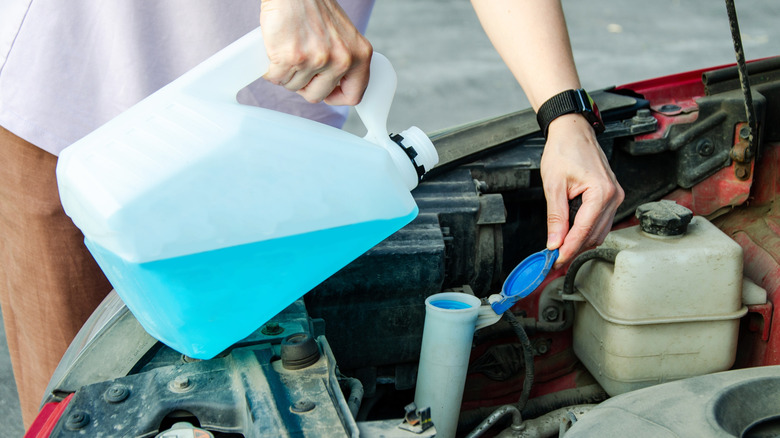 Blue windshield washer fluid being poured into a washer fluid reservoir.