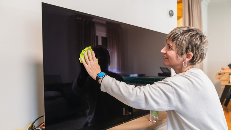 A person cleaning a TV screen with a microfiber cloth