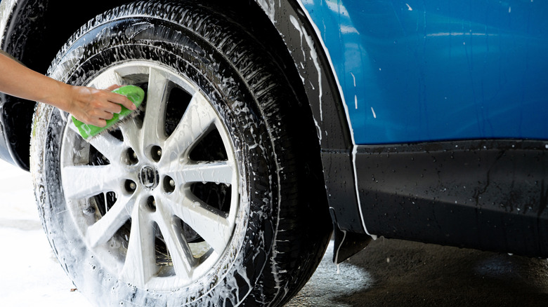 Hand holding sponge cleaning car tire