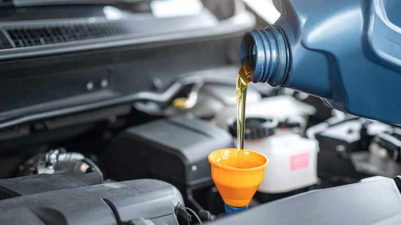 Engine oil is poured from blue bottle into car engine via yellow funnel