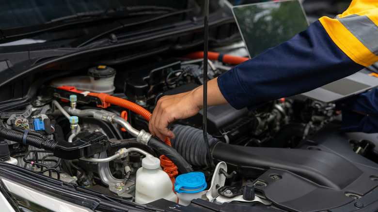 Mechanic's hand touches orange tube in engine bay under car's hood