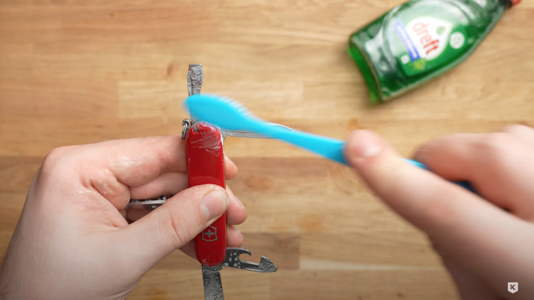 person cleaning swiss army knife with tooth brush