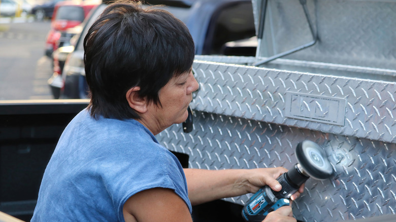 Woman Polishing Aluminum Toolbox with Power Tool While Sitting in a Truck Bed.