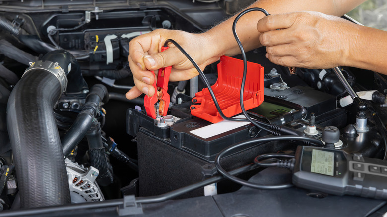 A person checks a car battery with an electric meter