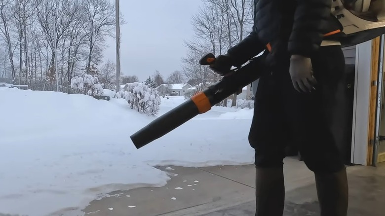 A person using a backpack blower to remove snow from a driveway.