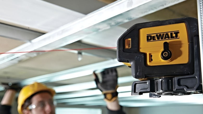 DeWalt laser level attached to wall while emitting red light as construction worker straightens item in background